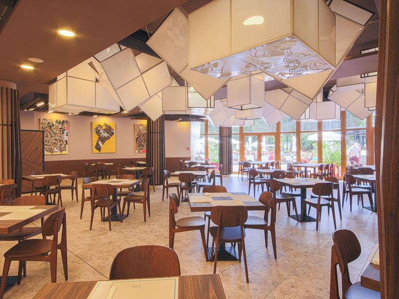 Helles, modernes Restaurant mit Holzstühlen, Tischen und dekorativen Deckenlampen.