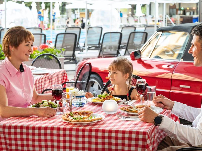 Familie sitzt an einem Tisch mit rot-weiß kariertem Tischtuch und genießt Mahlzeit im Freien.