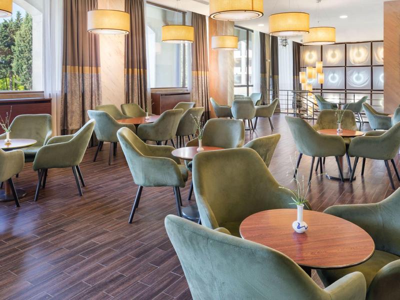 Moderner, heller Hotel-Lounge-Bereich mit grünen Stühlen und runden Holztischen.