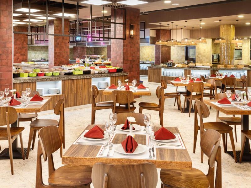 Moderner Hotelrestaurant mit Holztischen, bestückten Weingläsern und roter Tischdekoration.