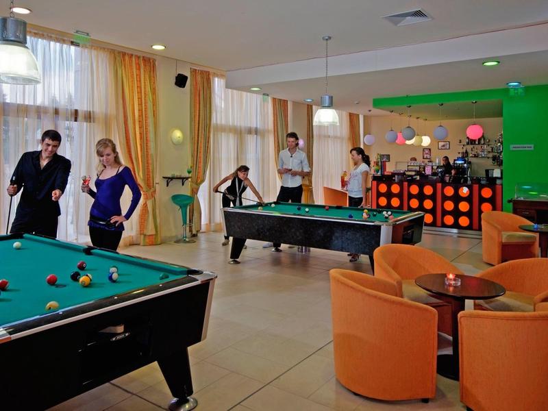 Freizeitbereich mit Billardtischen, orangefarbenen Sesseln und mehreren Menschen in einem hellen Raum.