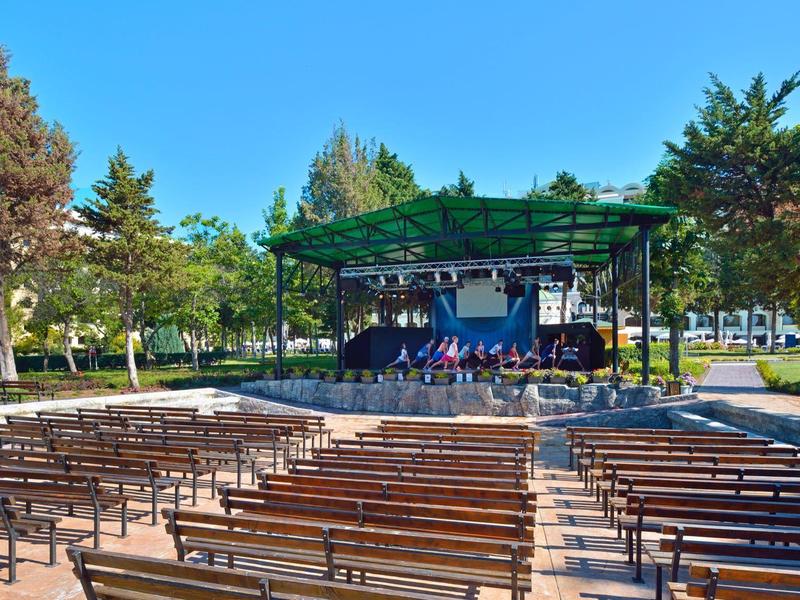 Leere Freiluftbühne mit Holzbänken und grüner Pergola in einem sonnigen Park