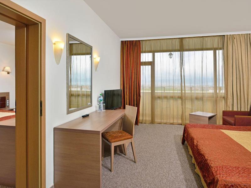 Modern eingerichtetes Hotelzimmer mit Bett, Schreibtisch, Stuhl und Sitzbereich vor großem Fenster.