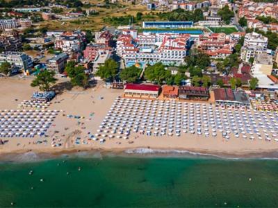 Luftaufnahme eines belebten Strandes mit Sonnenschirmen und Gebäuden im Hintergrund.