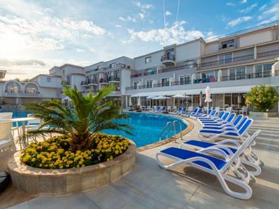 Hotelpool mit blauen Liegestühlen und Palmen unter blauem Himmel.