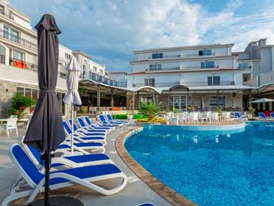 Poolbereich mit blauen Liegestühlen und Sonnenschirmen vor einem Hotel unter bewölktem Himmel.
