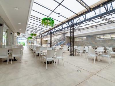 Helle, moderne Glasdach-Terrasse mit weißen Stühlen und Tischen in elegantem Restaurant.