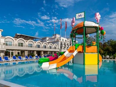 Bunter Wasserrutschen-Spielplatz neben Pool mit Liegestühlen und Gebäude im Hintergrund.