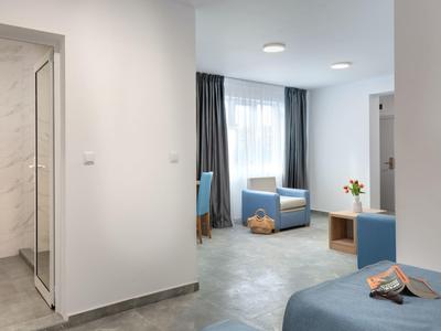 Modern eingerichtetes Hotelzimmer mit blauer Sitzgruppe, Bett und Arbeitsbereich bei natürlichem Licht.