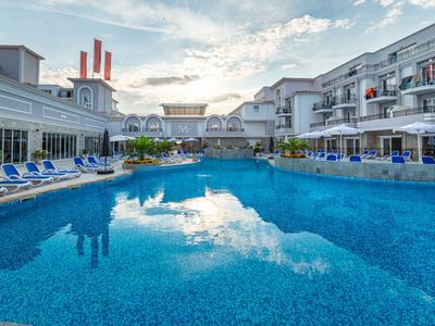 Moderner Hotelpool mit blauen Liegestühlen und zwei Gebäudeflügeln bei Sonnenuntergang.