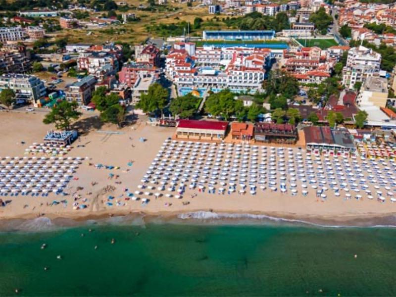 Luftaufnahme eines belebten Strandes mit Sonnenschirmen und Gebäuden im Hintergrund.
