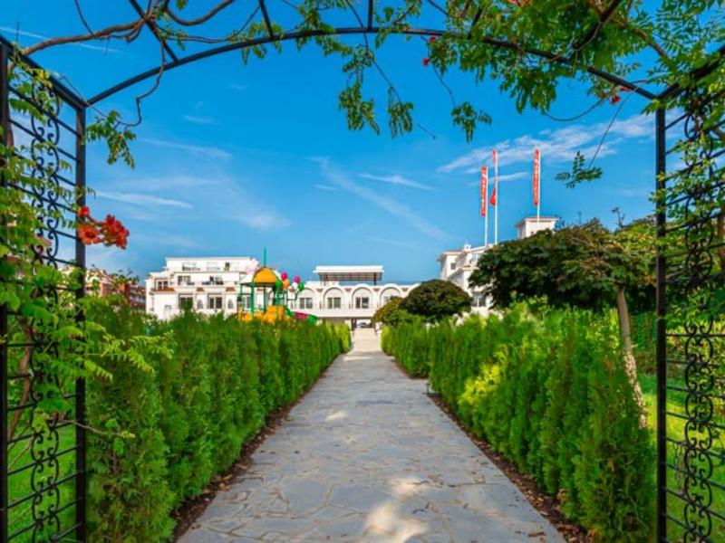 Ein gepflasterter Weg führt durch grüne Hecken zu einem modernen Hotelgebäude unter blauem Himmel.