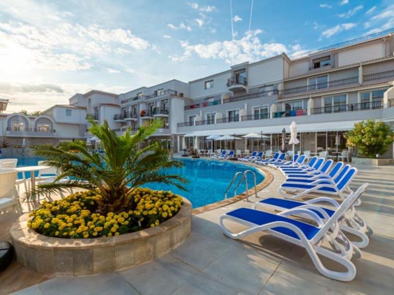 Hotelpool mit Liegestühlen und blühender Bepflanzung unter blauem Himmel.