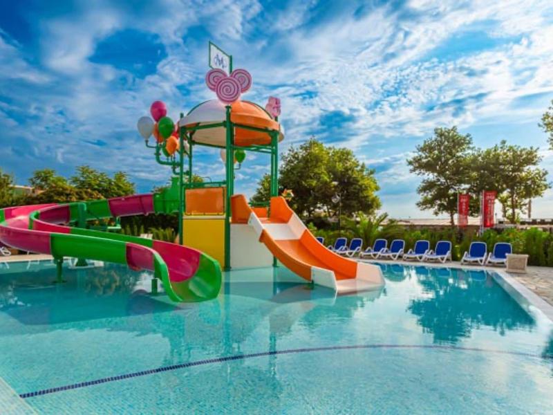 Bunter Wasserspielplatz mit Rutschen und Herz-Dekor in einem Hotelpool unter blauem Himmel.