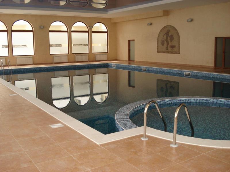 Innenpool mit rechteckigem und rundem Bereich in einem hellen Raum mit großen Fenstern