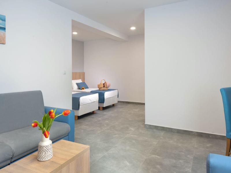 Moderner Hotelzimmerbereich mit Sofa, Sesseln und Betten in heller Einrichtung.