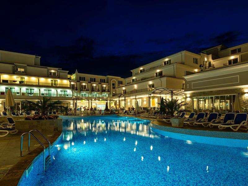 Beleuchtetes Hotel mit großem Pool und Liegestühlen bei Nacht.