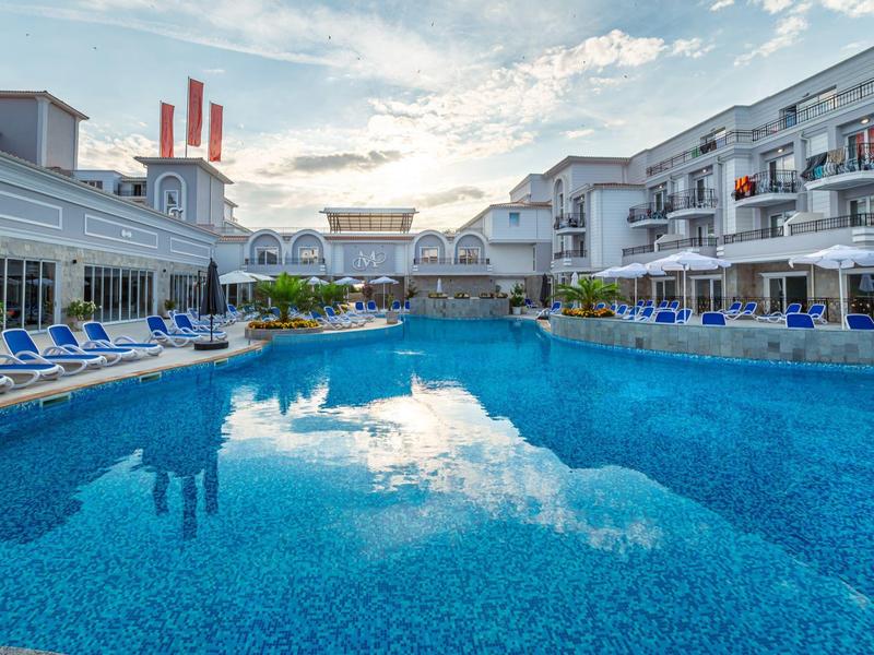 Großer Außenpool mit Liegestühlen in einem modernen Hotelkomplex bei Sonnenuntergang.