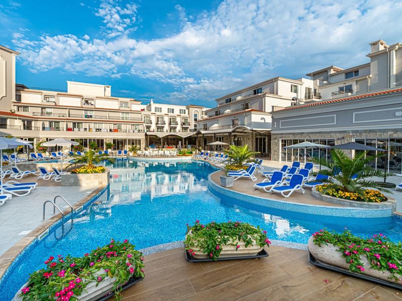 Großer Hotelpool mit Liegestühlen und blauen Sonnenschirmen unter blauem Himmel.