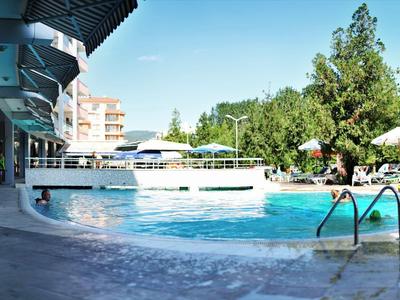 Area piscina esterna di un hotel con ombrelloni e verde sotto un cielo limpido