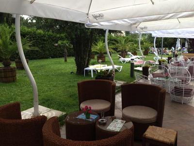 Area esterna di un caffè con sedie e tavoli sotto ombrelloni su una terrazza accanto a un giardino verde.