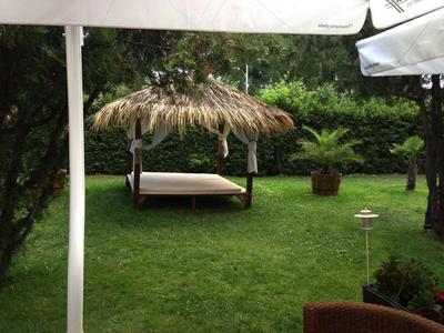 Giardino verde con prato, piante e un lettino coperto con tetto di paglia