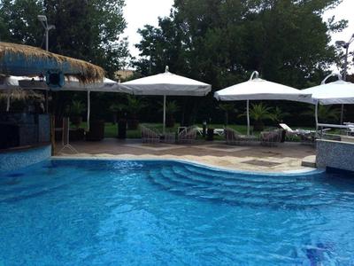 Zwembad met blauw water, parasols en groene bomen op de achtergrond.