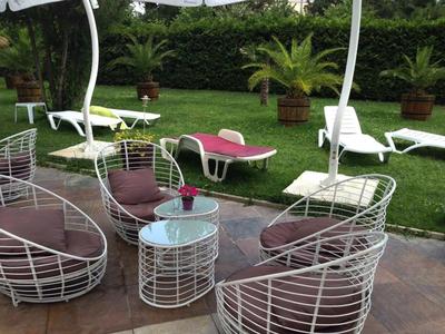 Witte metalen stoelen met paarse kussens en een glas op een ronde tafel naast ligstoelen in de tuin.