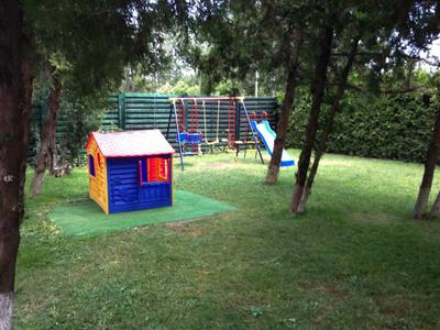 Kleine tuin met kinderspeelhuisje, glijbaan en grasveld met bomen.