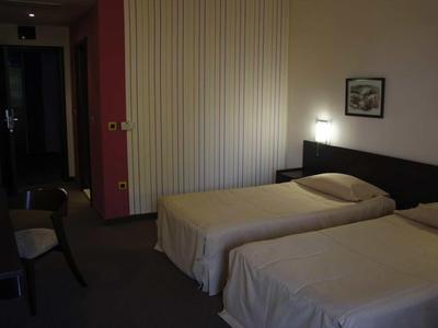 Donkere hotelkamer met twee eenpersoonsbedden, stoelen en een schilderij aan de muur.