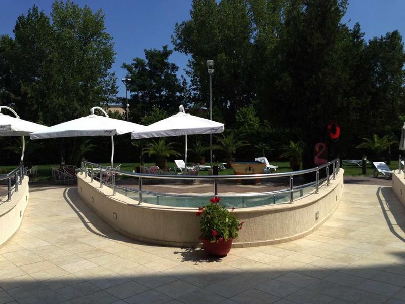 Klein rond hotelzwembad met parasols en ligstoelen, omgeven door bomen.