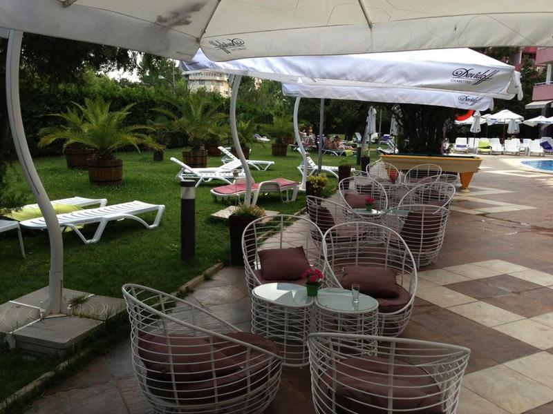 Terras met witte metalen stoelen en parasols naast ligstoelen op gras