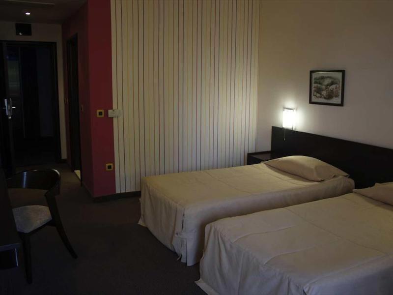 Donkere hotelkamer met twee eenpersoonsbedden, stoelen en een schilderij aan de muur.