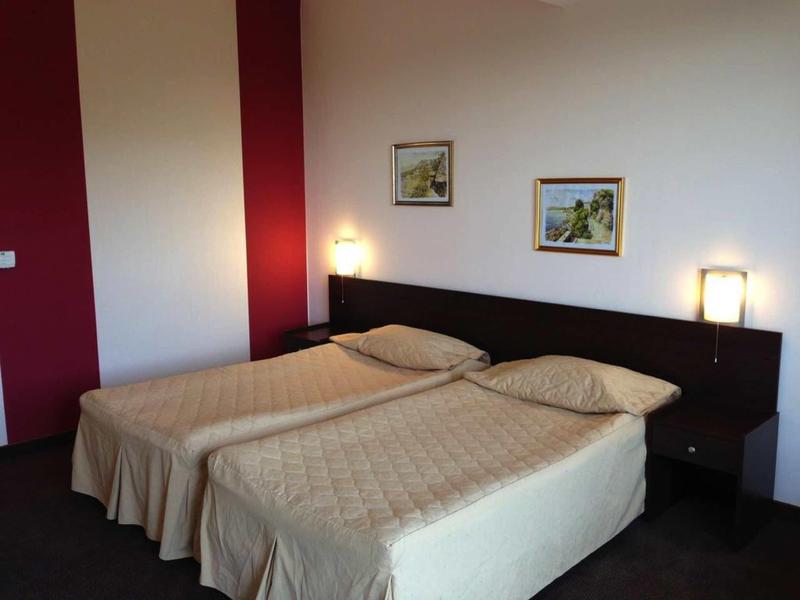 Twee eenpersoonsbedden met crèmekleurige dekens in een eenvoudige hotelkamer met donkere meubels.