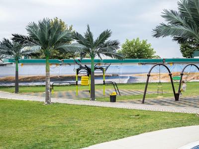 Een zwembadomgeving met palmbomen, schommels en ligstoelen onder een bewolkte hemel.