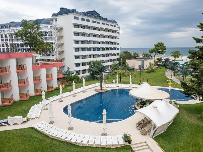 Buitenzwembad met ligstoelen voor meerdere meerlaagse hotels en de zee op de achtergrond.