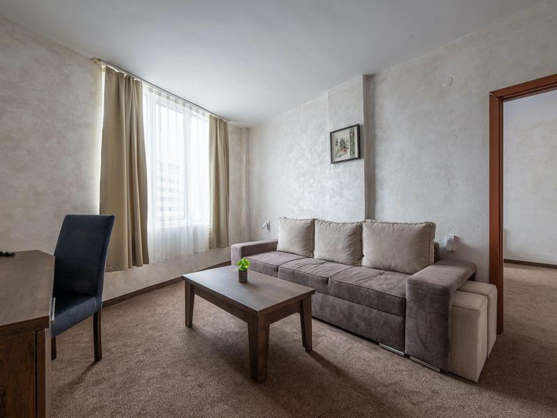 Licht gemeubileerde woonkamer met bank, salontafel en groot raam in een hotelkamer.