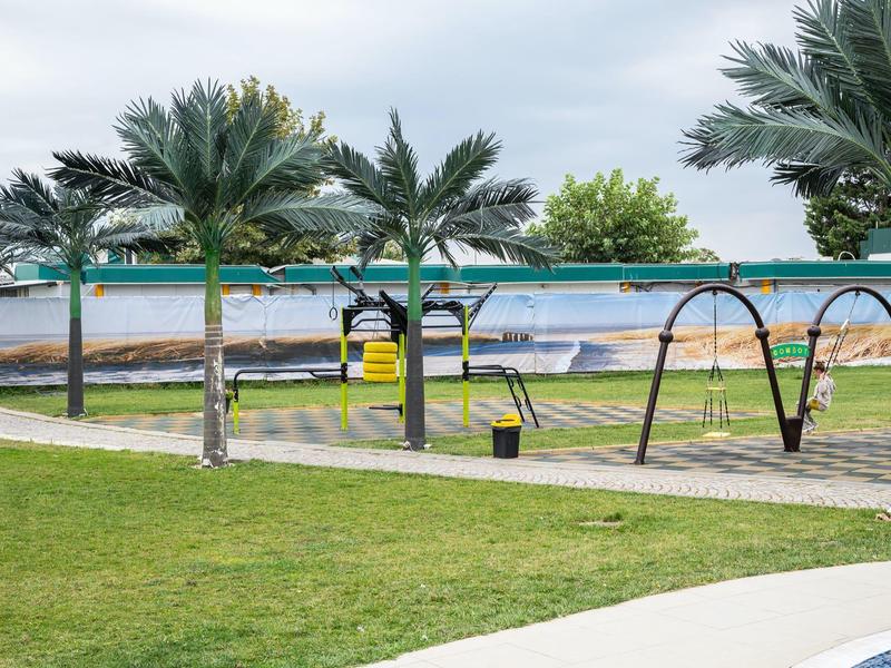 Een zwembadomgeving met palmbomen, schommels en ligstoelen onder een bewolkte hemel.