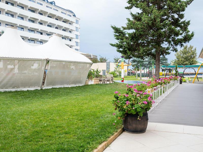 Groen gazon naast wandelpad met witte tenten en meerlaagse hotel op de achtergrond.