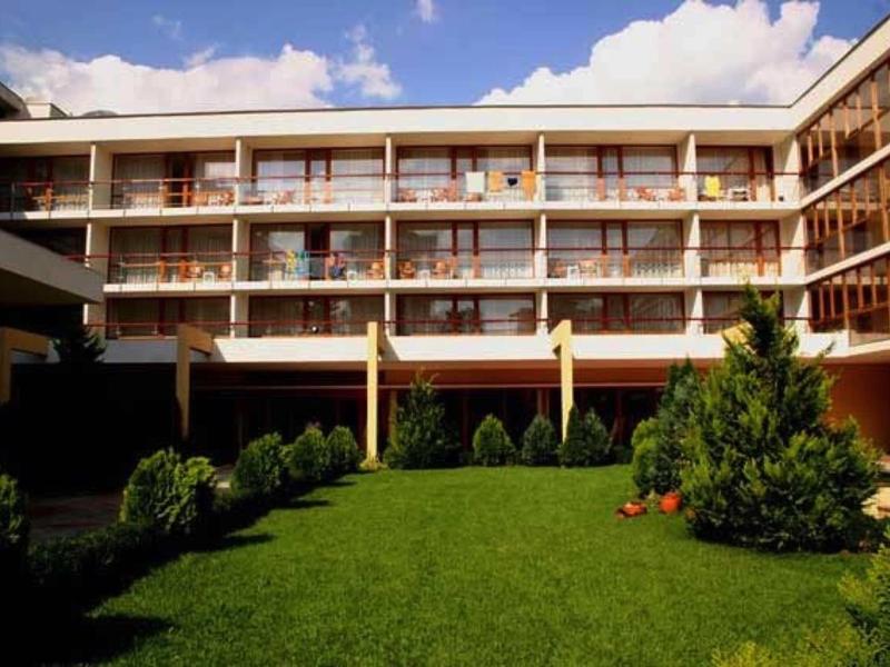 Modern hotelcomplex met groen gazon en meerdere balkons onder een zonnige hemel.