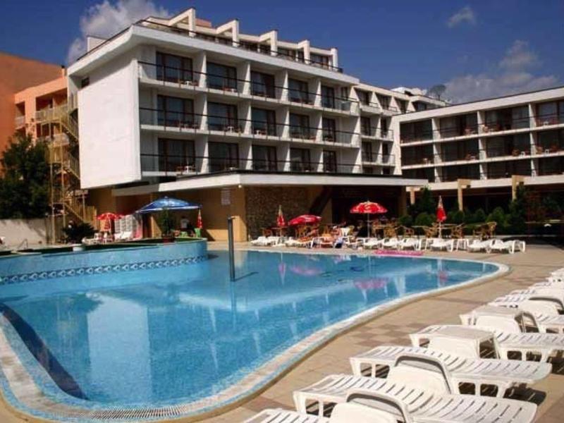 Hotel met groot buitenzwembad, ligstoelen en rode parasols bij heldere lucht.