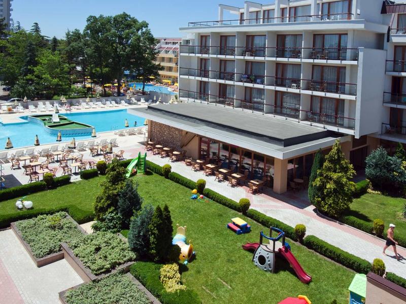 Hotel met buitenzwembad, ligstoelen en een speeltuin in het groene tuingebied.