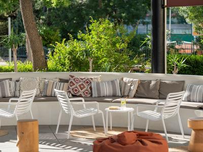 Gemütliche Outdoor-Lounge mit weißen Stühlen und großer halbkreisförmiger Couch bei Tageslicht.