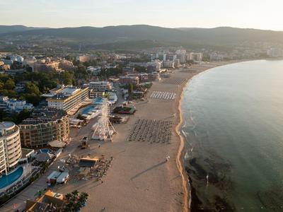 Luftaufnahme eines breiten Sandstrands mit Hotels und Stadt im Hintergrund bei Abendlicht