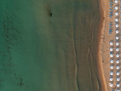 Luftaufnahme eines Strandes mit Reihen von Sonnenschirmen und klarem blau-grünem Wasser.