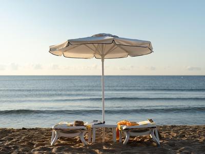 Zwei Liegestühle mit Handtüchern und ein Sonnenschirm am ruhigen Strand mit Blick auf das Meer.