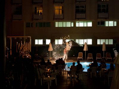 Beleuchteter Poolbereich eines Hotels bei Nacht mit Gästen und Sonnenschirmen.