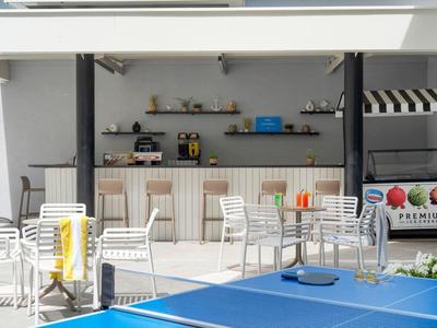 Freizeitbereich mit Tischtennisplatte, weißen Stühlen und Bar mit Getränken im Hintergrund.