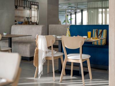 Heller, moderner Frühstücksraum mit Holzstühlen, weißen Kissen und grauen Sitzbänken.