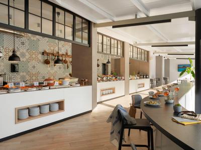 Moderner Frühstücksbereich mit langem Tisch, Stühlen und Buffet in einem hellen Raum.